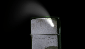 A zippo style lighter, engraved with "Forever yours, Alodie". A white flare is seen leading upwards from the closed lid.