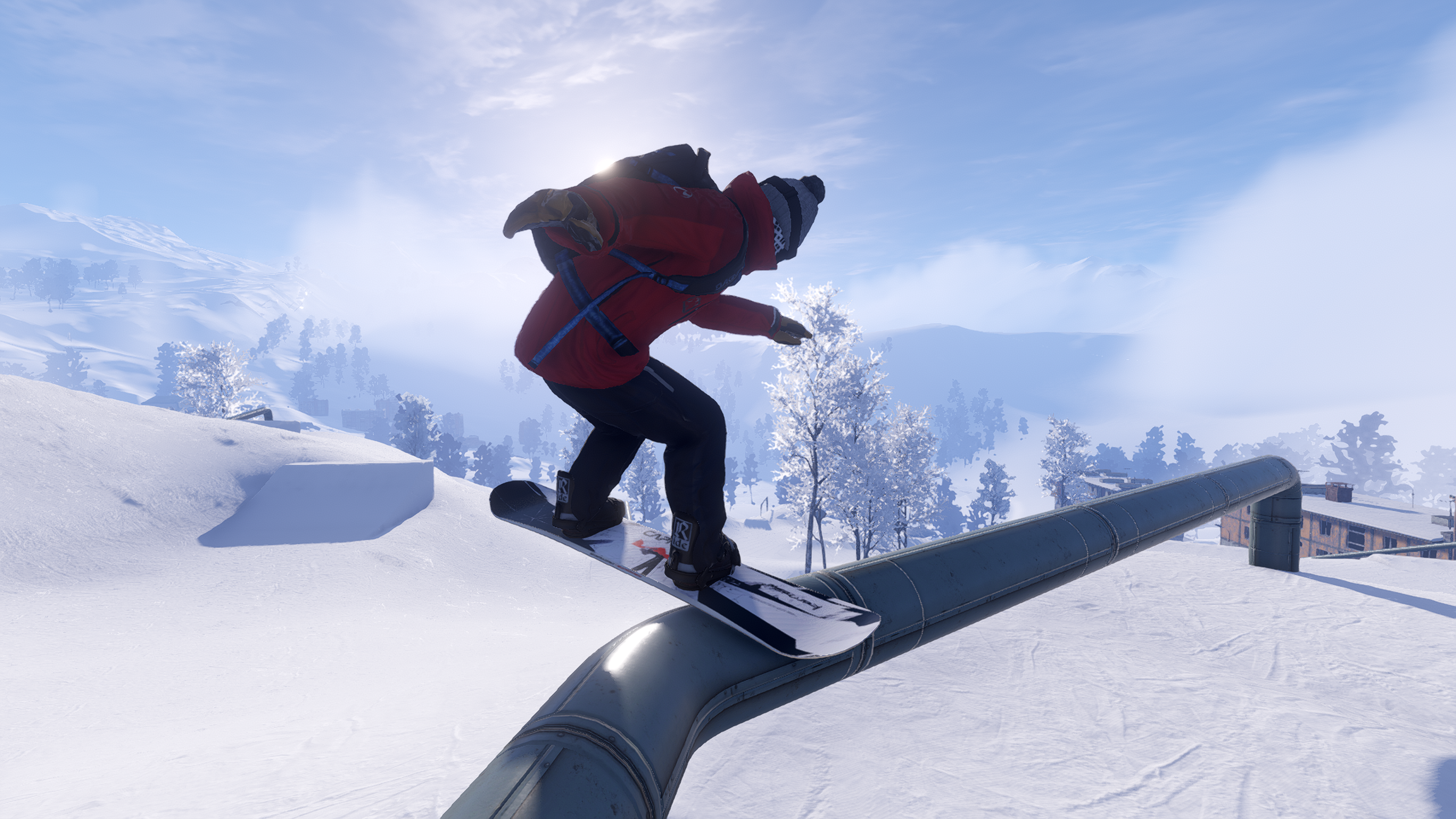 a closeup from behind a snowboarder as they grind on a metal pipe. The snowboarder is wearing a red jacket, black trousers and a grey bobble hat. The board they are riding on is whit with a black and red pattern on it. The mid-ground in front of the snowboarder features snow covered trees and buildings. The sun peers over the top of the snowboarders black backpack that they are carrying on their back