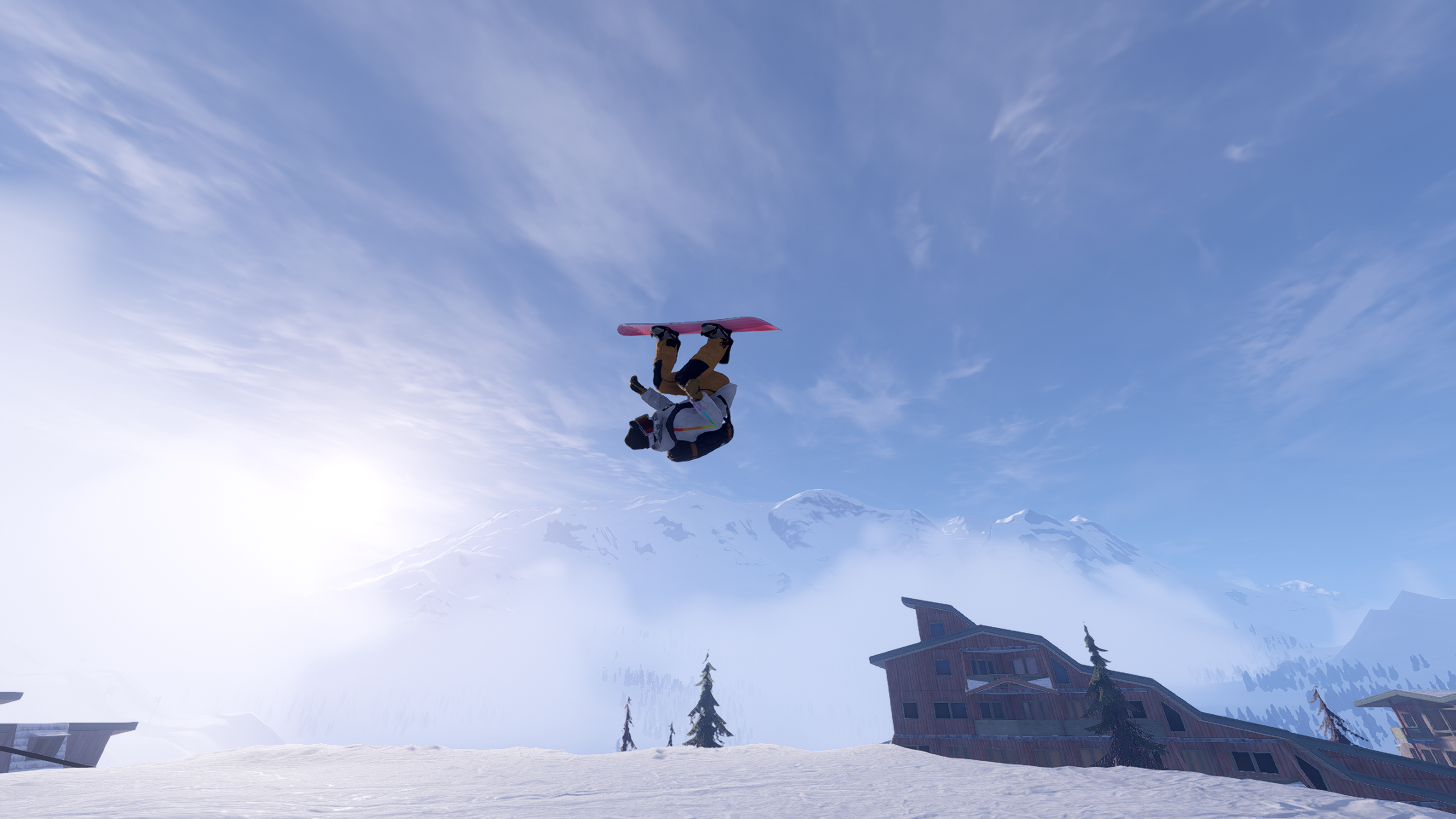 A snowboarder performs a front flip and are mid trick totally inverted mid air. They are riding on a red snowboard wearing a white jacket, mustard trousers and a black backpack on their back. The mid-ground behind the snowboarder has some multistory wooden lodge style buildings. The far background has some high rocky mountains covered in snow and engulfed in low lying cloud that the sun is shining through. 