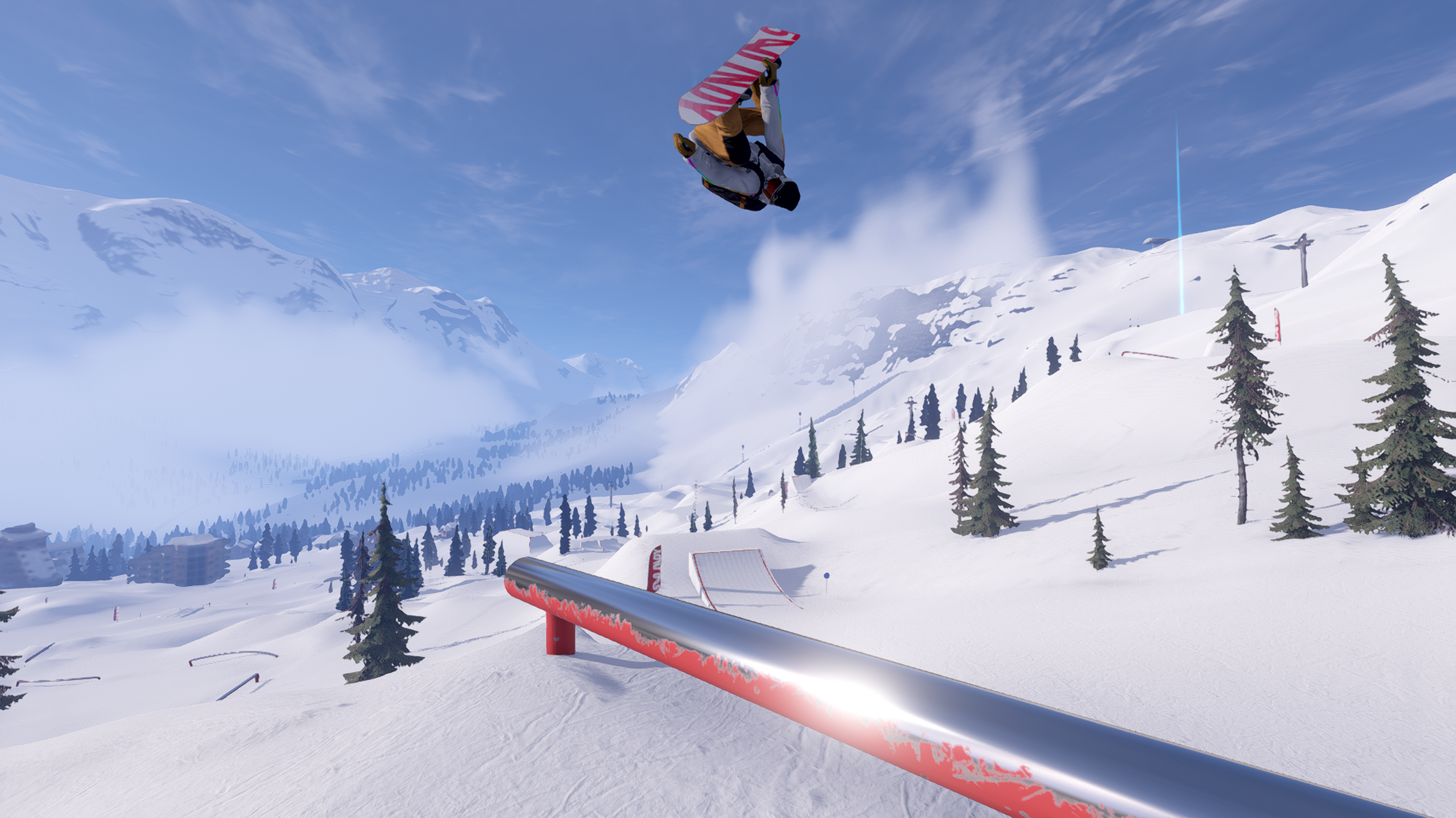 An snowboarder performing a front flip over a steel grind rail. The grind rail is read with the surface of the paint worn off down to a polished shiny steel. Dotted around the midground and background are some green trees. The background shows a valley with a large mountain to the left with som low lying cloud hovering down through the valley. The snowboarder is riding a white board with red text on the underside that reads "540 Indy"