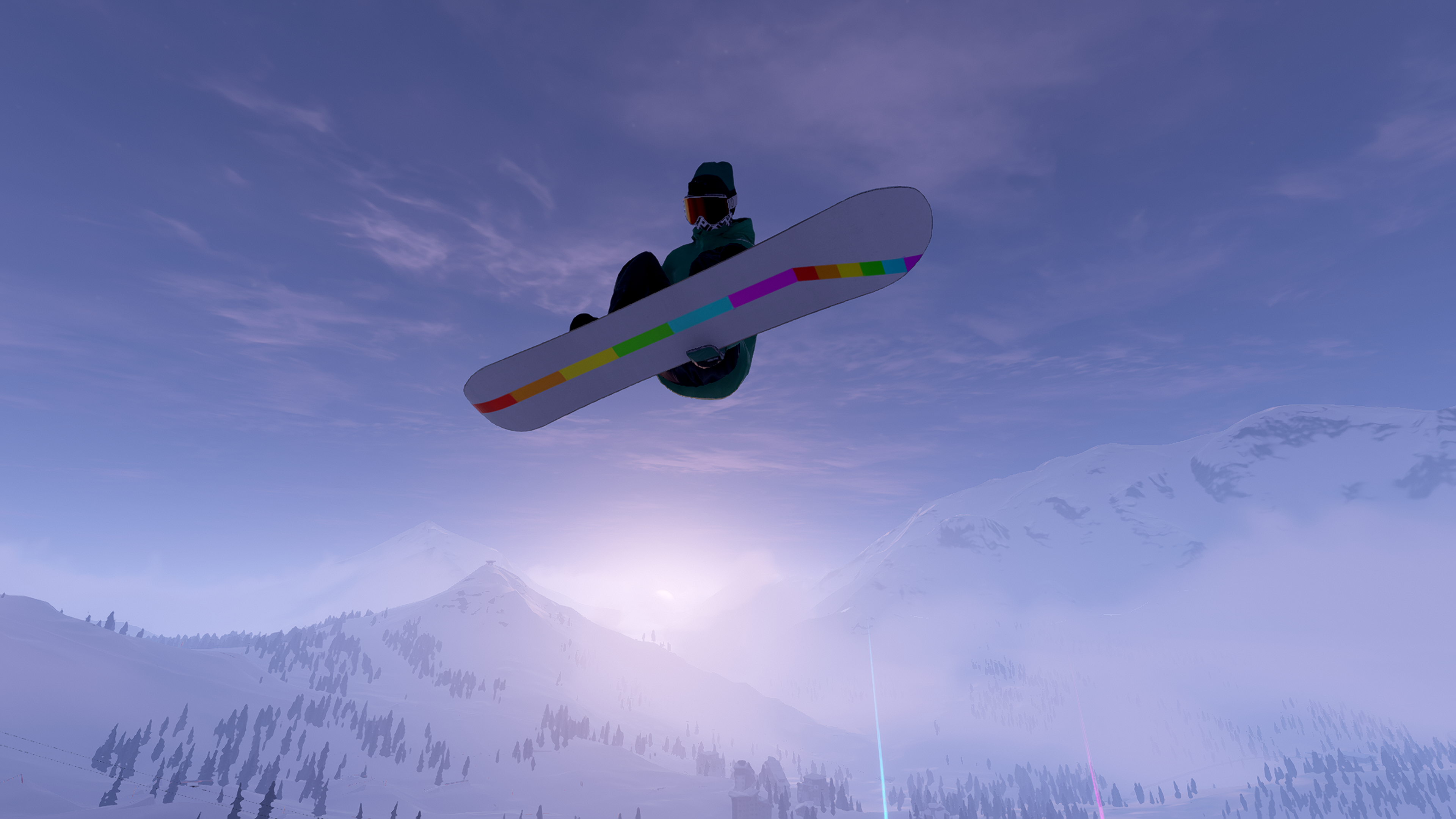 A snowboarder dressed in green jacket, green hat and black trousers jumps over the camera view on a white board featuring a rainbow coloured stripe on the underside. Sun blazes through snowy, tree covered mountains in the background with a blue sky above