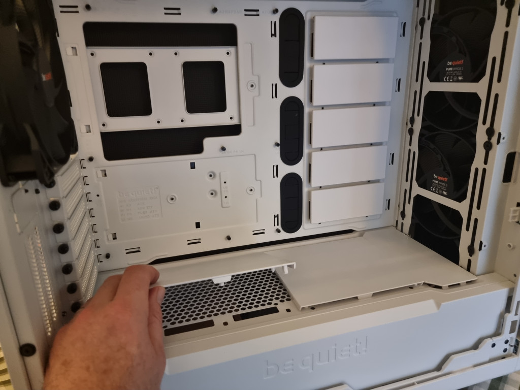 The photo shows the inside of the white pc case and the vast space there is to house the pc parts. The bottom tray is being removed to reveal the holes available for cable management as well as allowing airflow around the PSU.