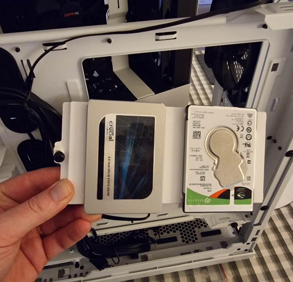 the photo shows an ssd and hdd mounted to a white metal tray that will be affixed into the pc case on tha cable management side.