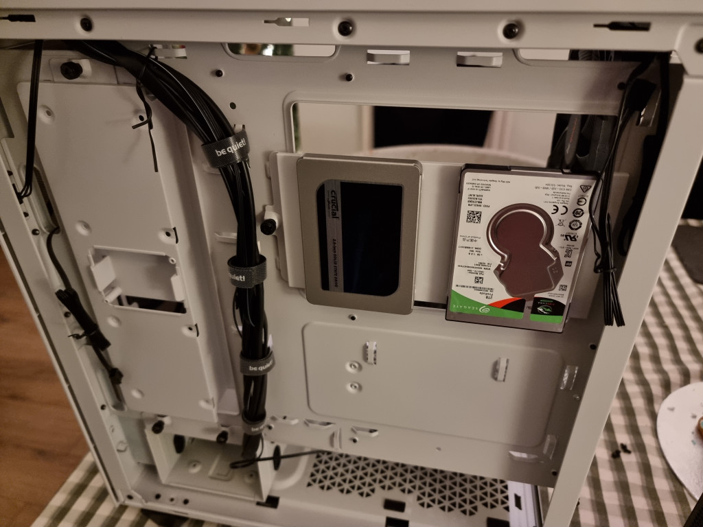 screenshot showing the inside of the pc from the right-hand side. 2 SSDs are shown attached to the white chassis by a simple frame and singular screw. A black run of cables is visible running neatly through the case and held with velcro. 