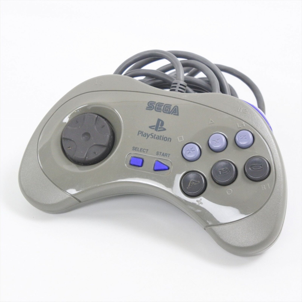 A sega playstation branded greay controller with 8 way directional buttons on the left, bles start & select buttons in the middle and a six button layout on the right - X, Y, Z buttons in light blue along the top and A, B, C buttons in dark grey bellow.