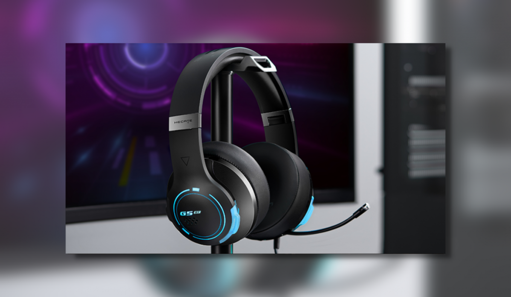 image showing a dark black headset with blue neon lit ear cups sitting on a small stand. Behind is a blurred purple monitor screen.