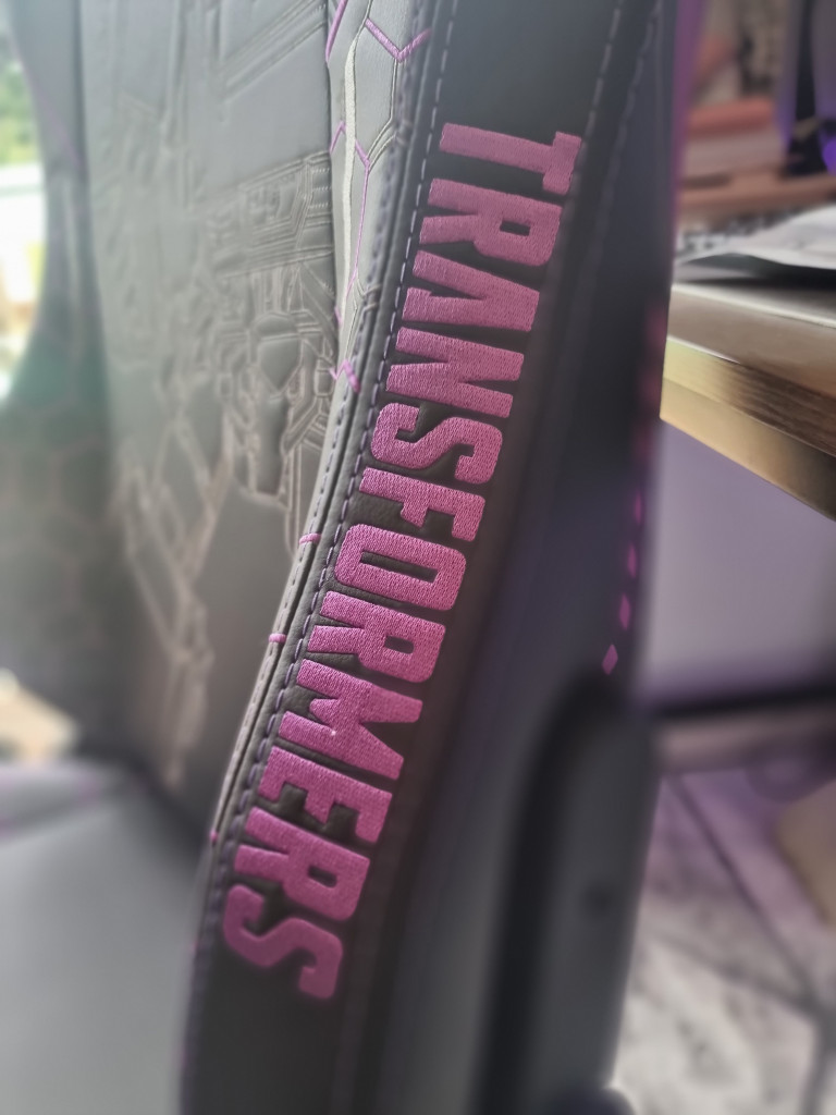 picture showing the word "Transformers" in purple stitching written down the side of the black gaming chair seat back.