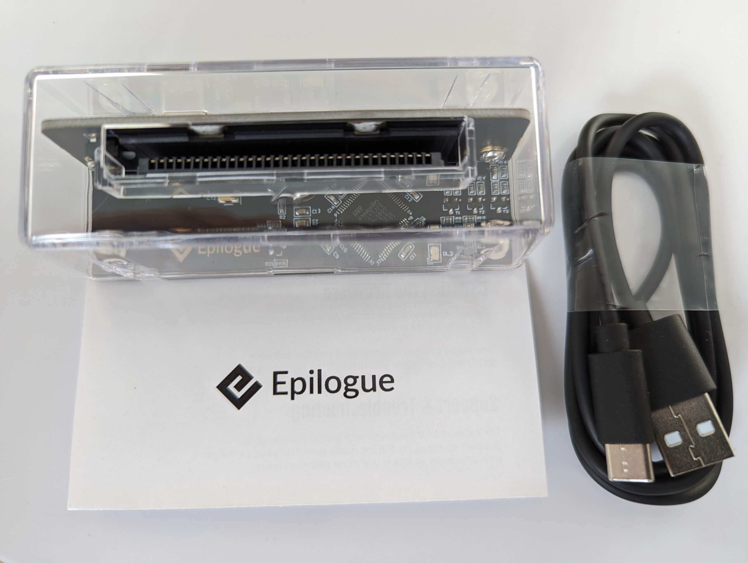 contents of the Epilogue GB Operator box showing the GB Operator device, a small white booklet with the Epilogue name and logo on it in black text, and a black USB-A to USB-C cable
