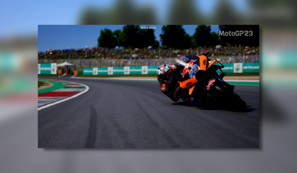 motorbike leaning into a corner with orange and black livery. The background is blurred due to depth of field effects so the crowd arent legible.