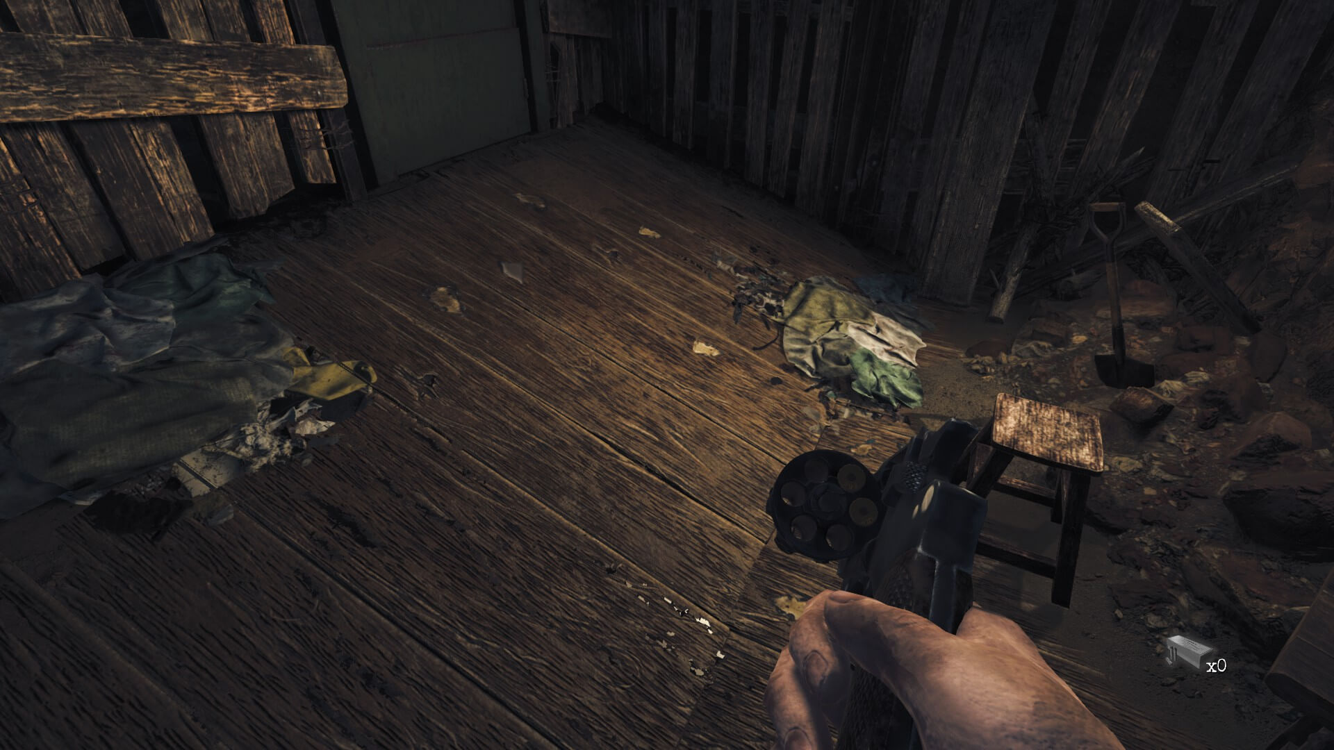 I am checking how many bullets are left in my revolver. several scraps of clothing can be seen on a table with a lonely chair besides it.
