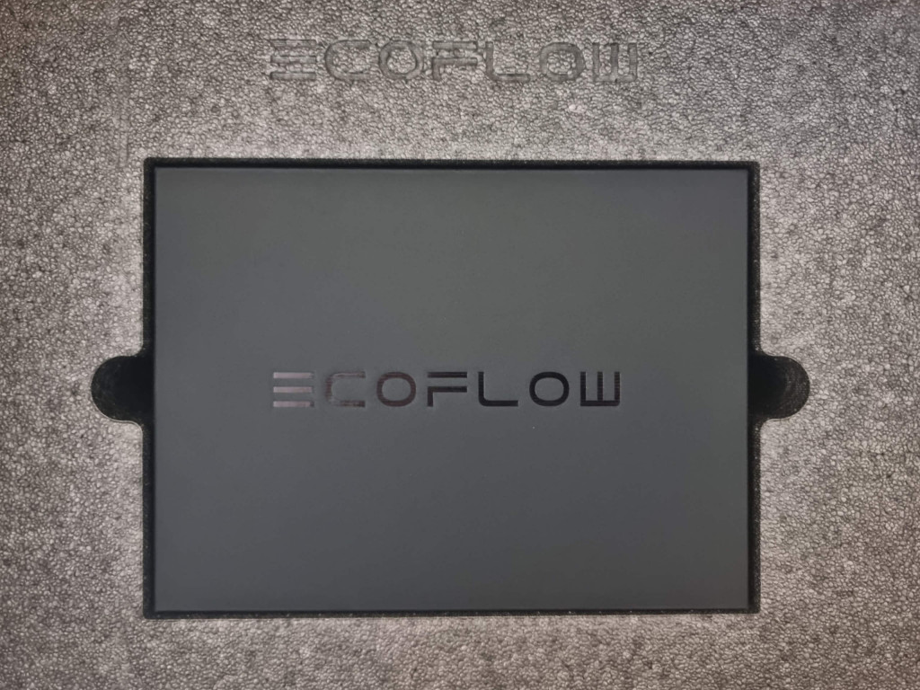 photo showing the a top down view of the contents of the box when you open it. Grey polystyrene encapsulates a black cardboard box that is nestled in the centre. The word "ecoflow" can be seen on the box.
