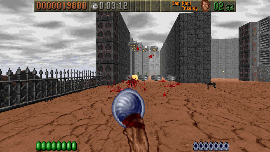 screenshot showing an fps view with a dark staff featuring a blue orb on the top as the weapon in use. Infront and in the air are the red bloody remains of enemy soldiers. The floor is light brown and cracked and the high walls behind are grey blocks.