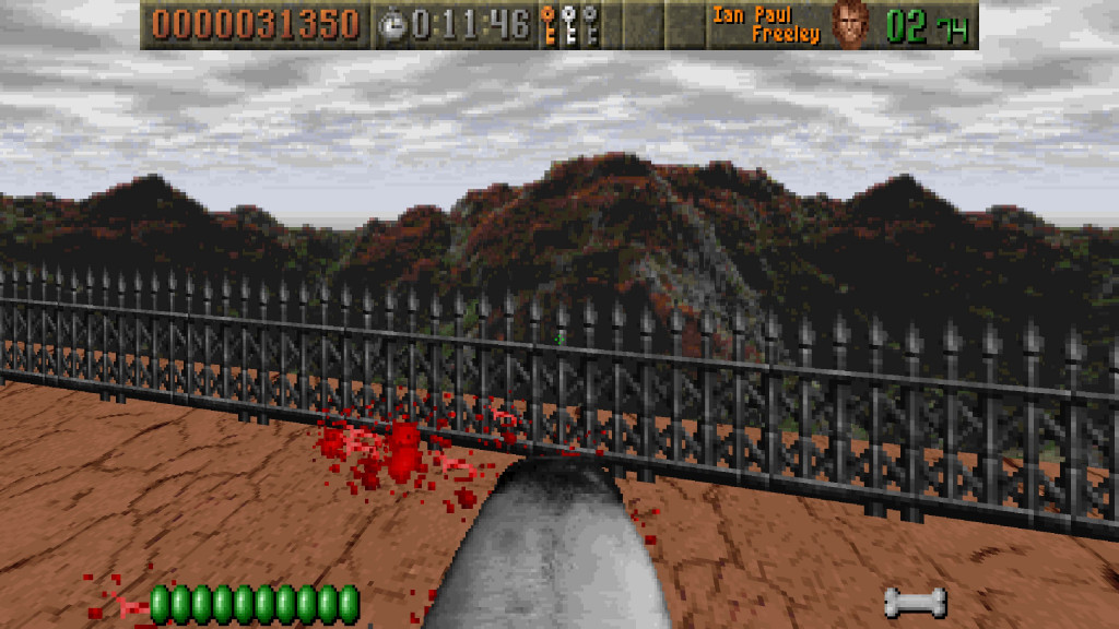 screenshot showing an fps view with dog mouth as the weapon in use. Infront and in the air are the red bloody remains of enemy soldiers. The floor is light brown and cracked and there is a metal railing with a mountain range and grey skies behind.