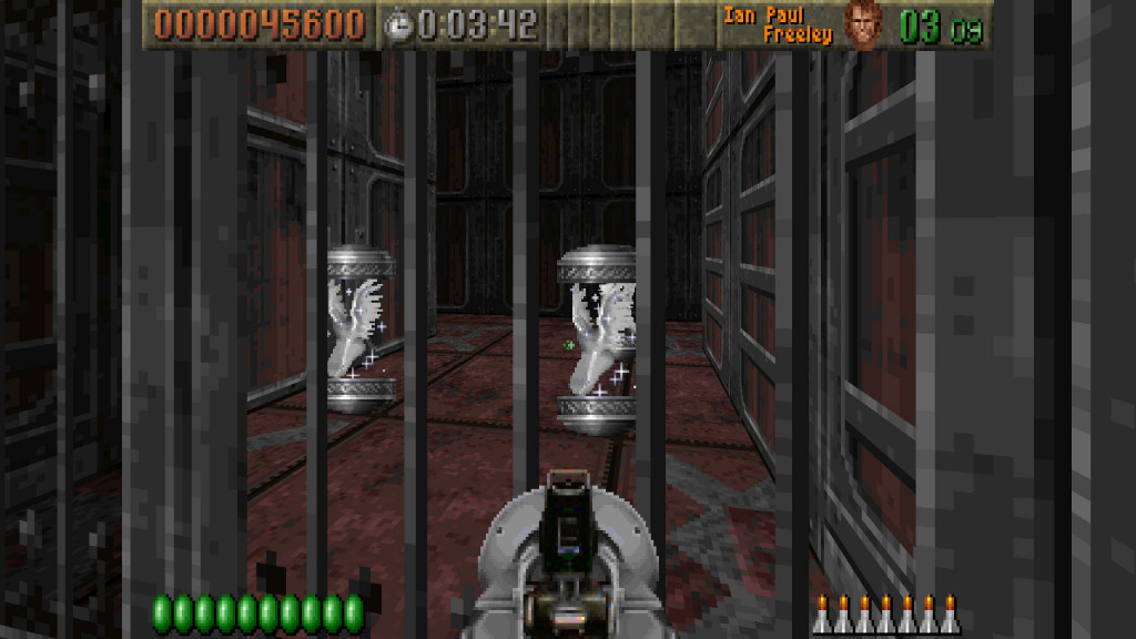 screenshot showing an fps view with a silver bazooka as the weapon in use. Infront are silver bars and behind are 2 flying power ups shown as white wings in a silver and glass capsule. The floor is pink slabs and the high walls behind are metallic blocks.