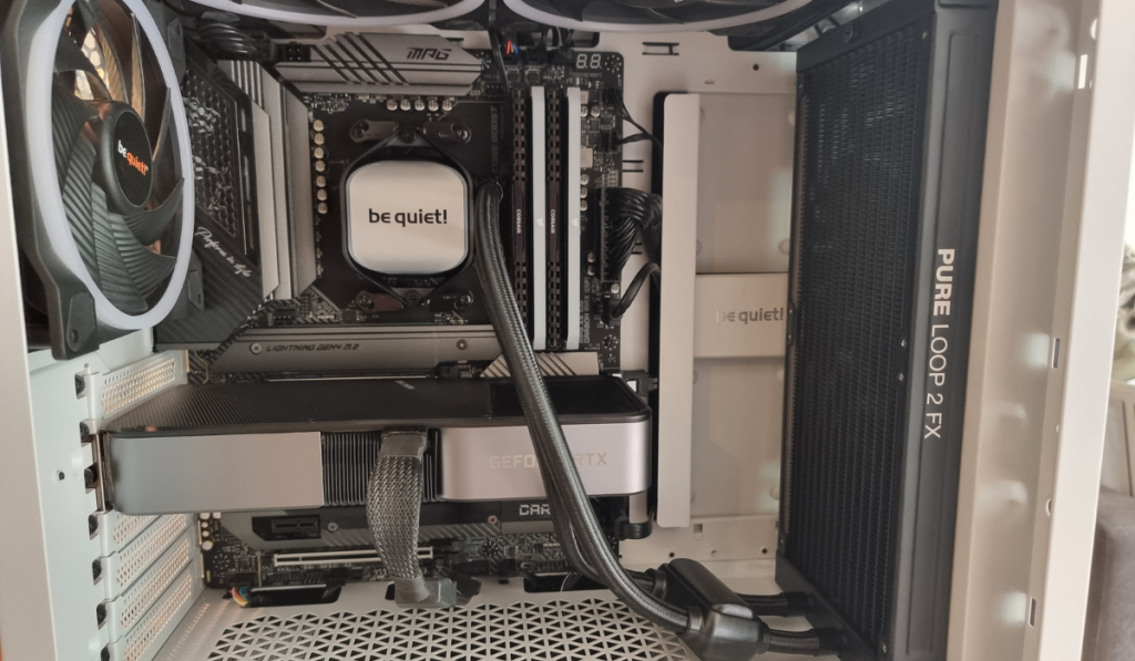 photo showing the completed installation of the AIO. The photo is similar to the previous one in that you can see the inside of the PC, this time with the silver and black be quiet cooler block in-situ along with the trailing black braided hoses going to the black radiator. It looks smart and super spacious.