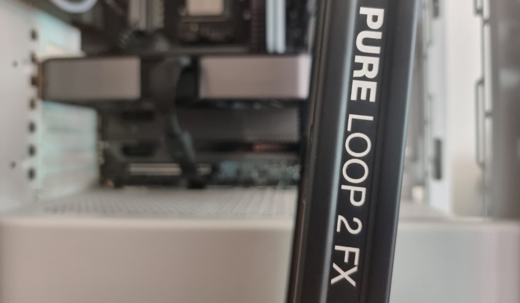photo showing the black radiator side on to the camera with white writing running down the side saying "Pure Loop 2 FX". In the background you can see a blurred white PC case and components, ready for the installation.