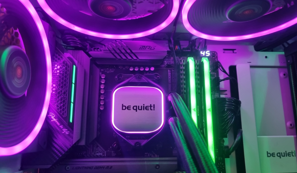 an intense photo showing the purple and green neon glow of the 3 exhaust fans and memory up close and personal with the silver cpu cooler block in the centre of the image illuminated in purple light.