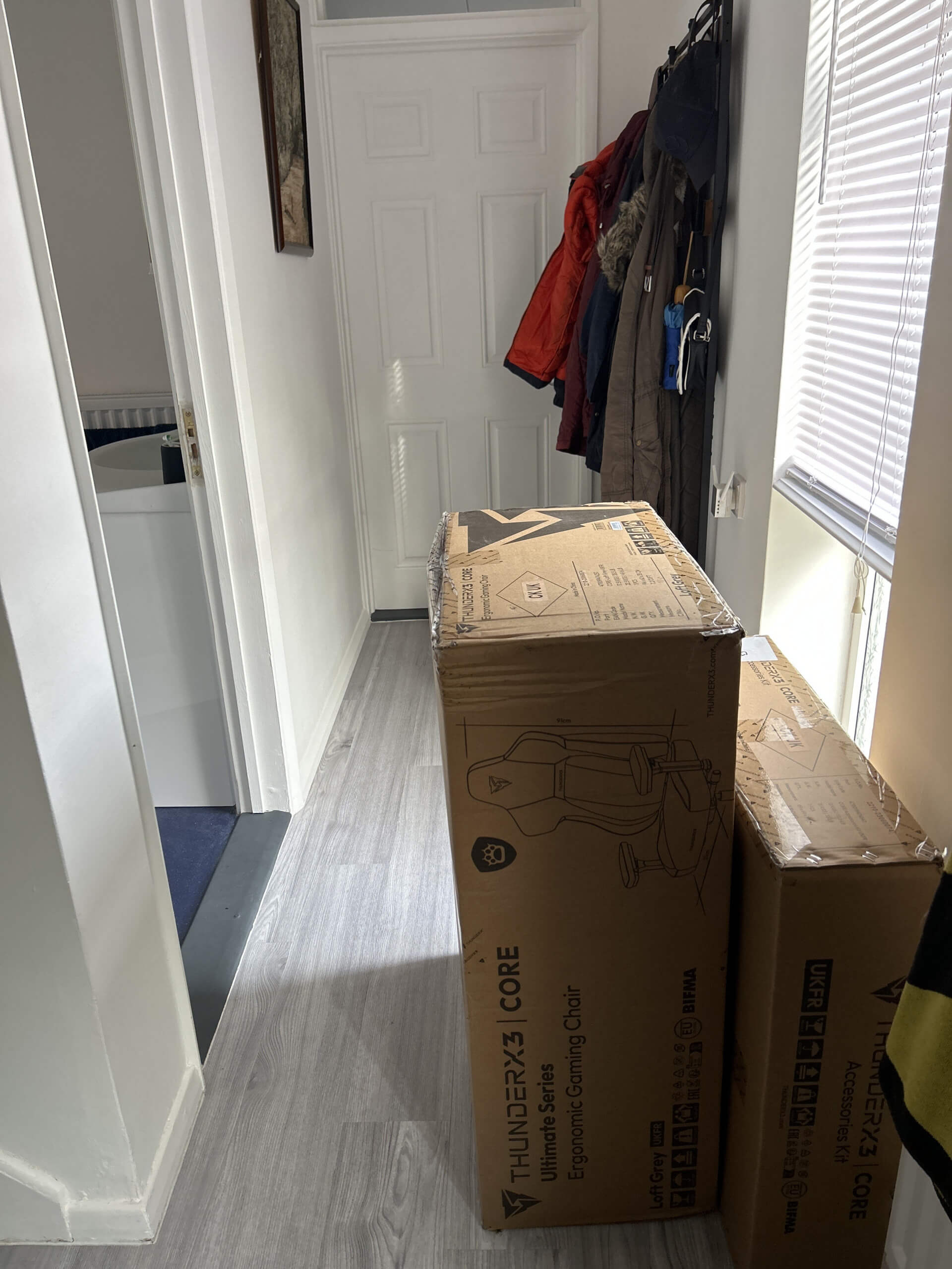 This photograph shows two carboard boxes in a hallway. These boxes have the gaming chair components inside. 