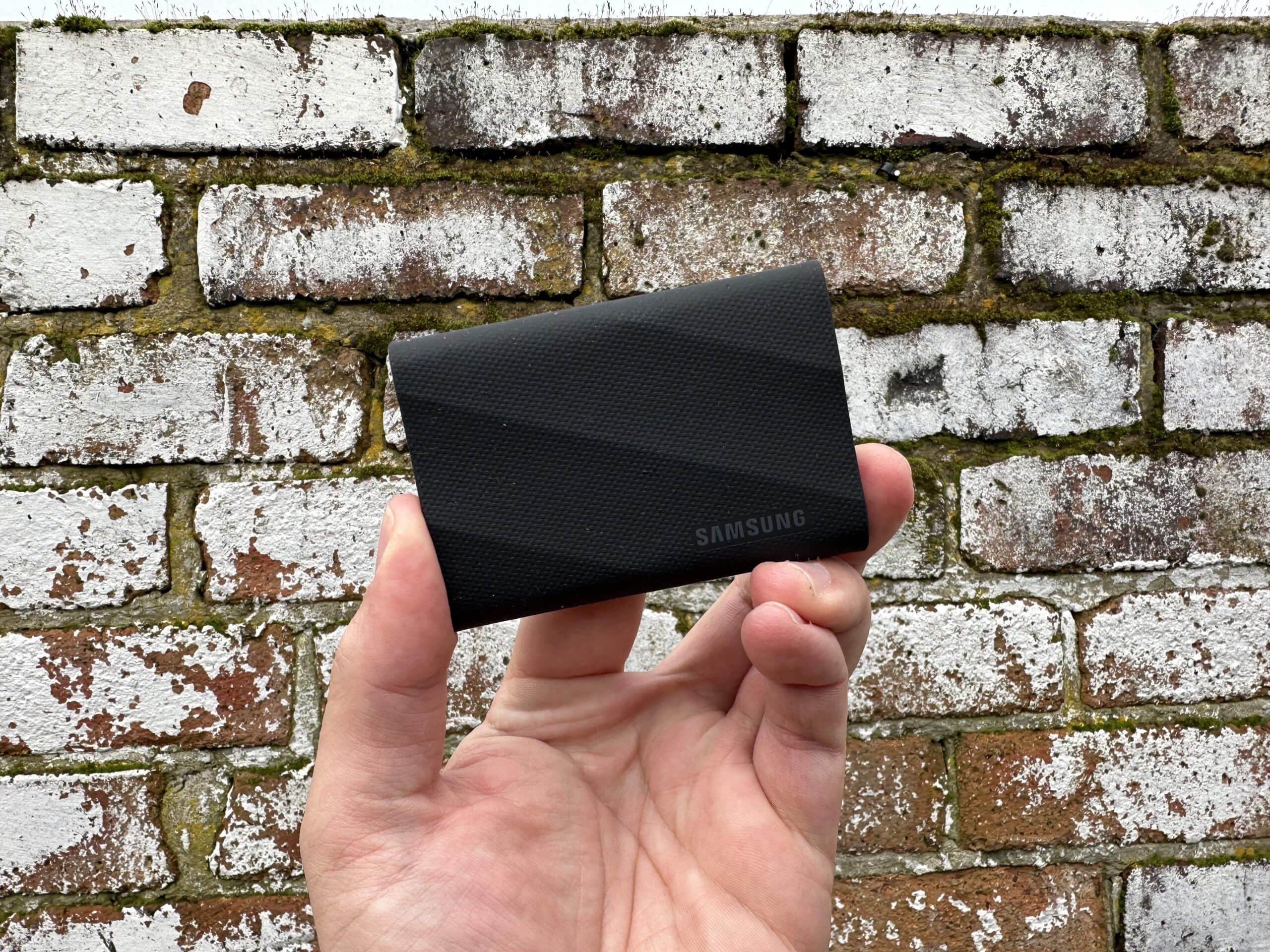 the samsung T9 portable SSD being held at fingertips in front of a brick wall