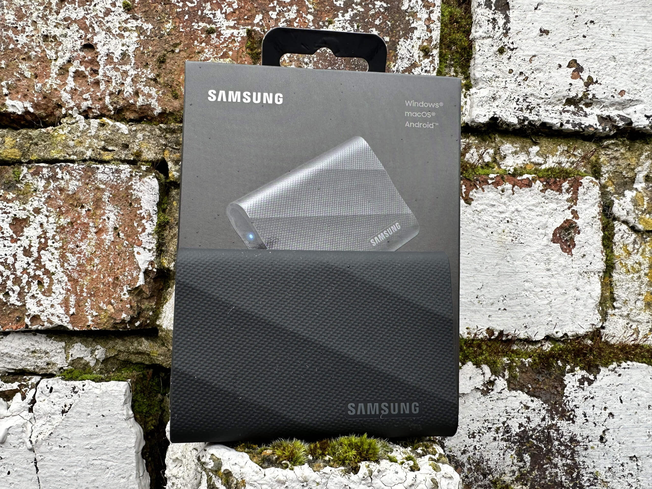 samsung t9 portable ssd unboxed sitting on a post in front of the box showing details of the ssd.