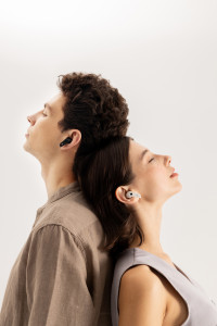 Two people are stood back to back, resting their heads against the other. The left, taller person is wearing the black NeoBuds Pro 2 earbuds, while the right, shorter person is wearing the white NeoBuds Pro 2 earbuds.