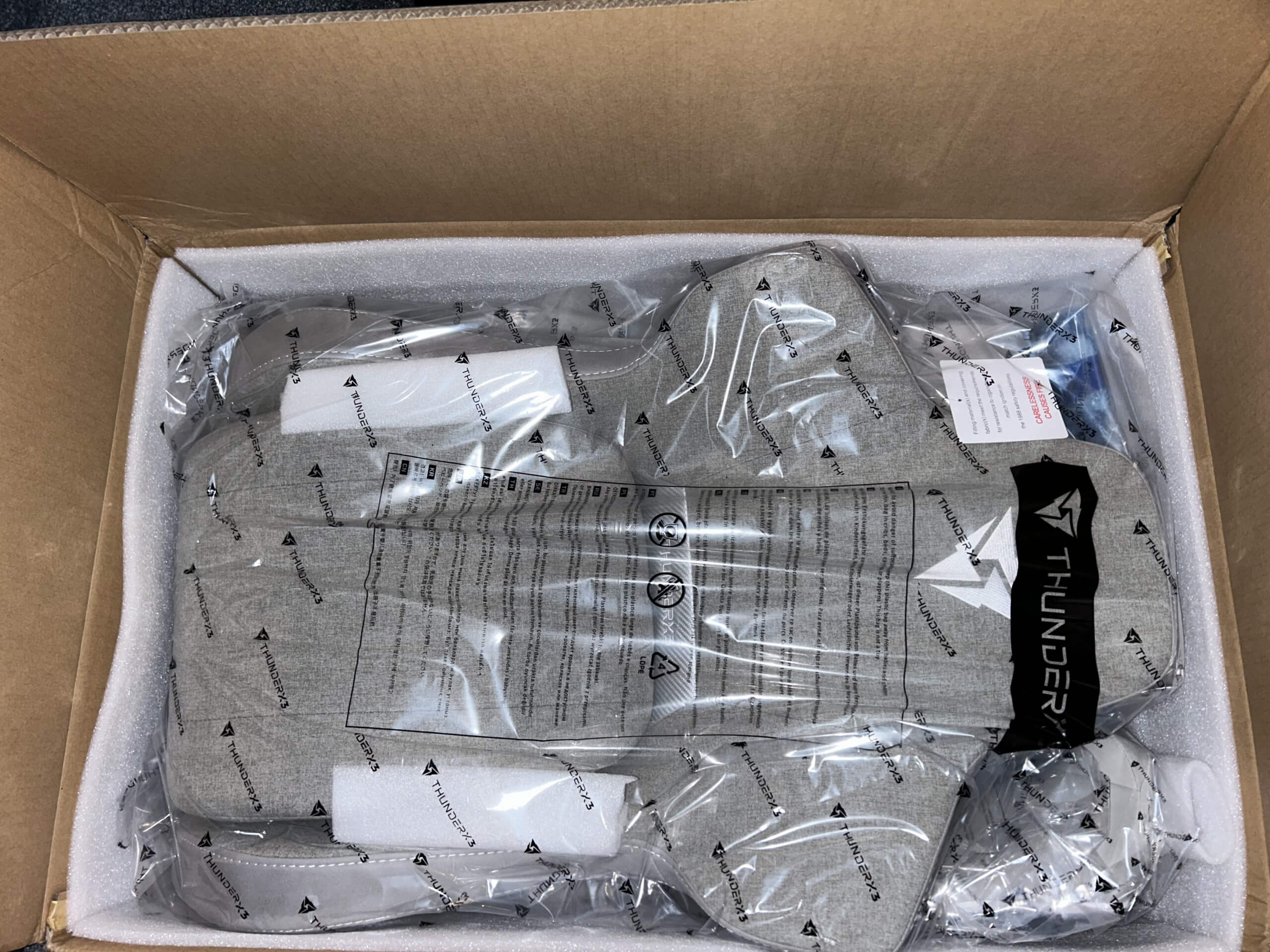 This photograph shows the chair when it was delivered in the boxes. Each piece is wrapped in plastic and bubble wrap. The chair is off a grey fabric colour. 