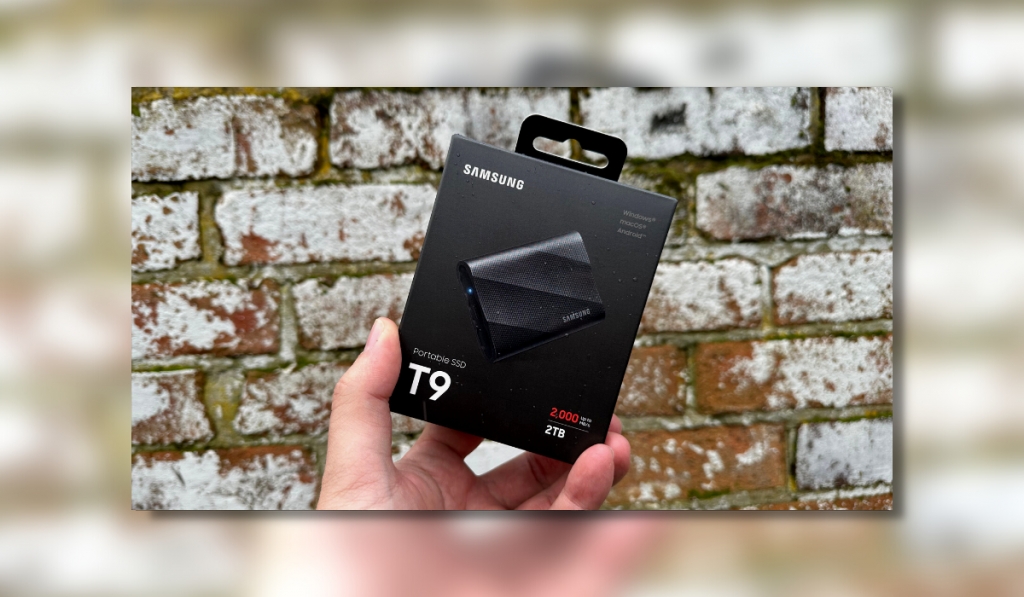 the samsung t9 box showing an image of the portable ssd being held by hand in front of a blurred brick wall