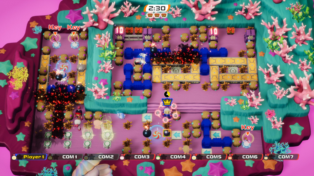 screenshot showing castle mode. the landscape is made up of a pink floor with darker pink rocks around the south and west. To the north and east is a raised green area. Nestled between there are 3 treasure chests that are being defended by White. There are brown round boulders to destroy as well as 7 AI bombermen dropping black bombs with flames coming from the top. 2 black and red explosions have cascaded through the screen from bomb explosions.