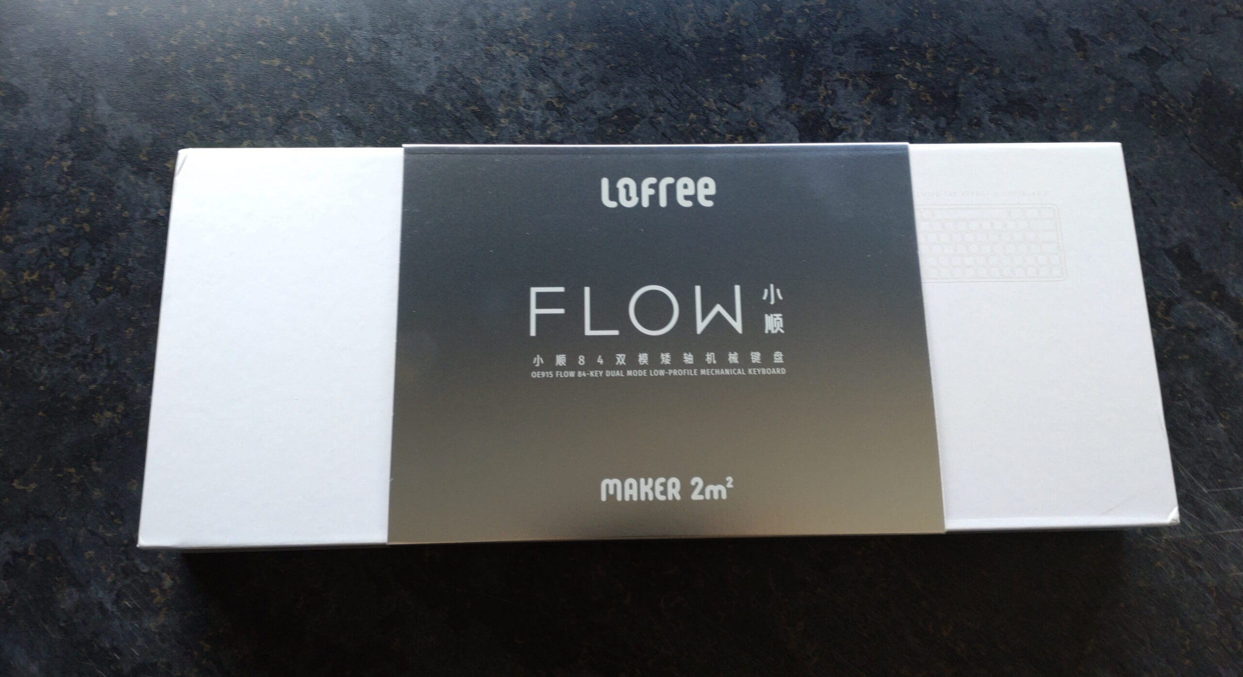 A white rectangular box with a silver sleeve around the middle of it. There is white text on the silver sleeve that says Lofree Flow.