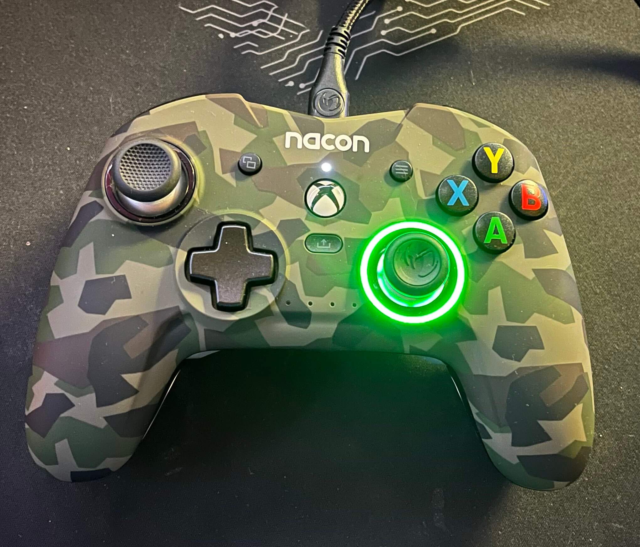 The Nacon Revolution X Pro controller has a lit right thumbstick that is green for normal profile. The camo is a dark brown, green, and tan design.