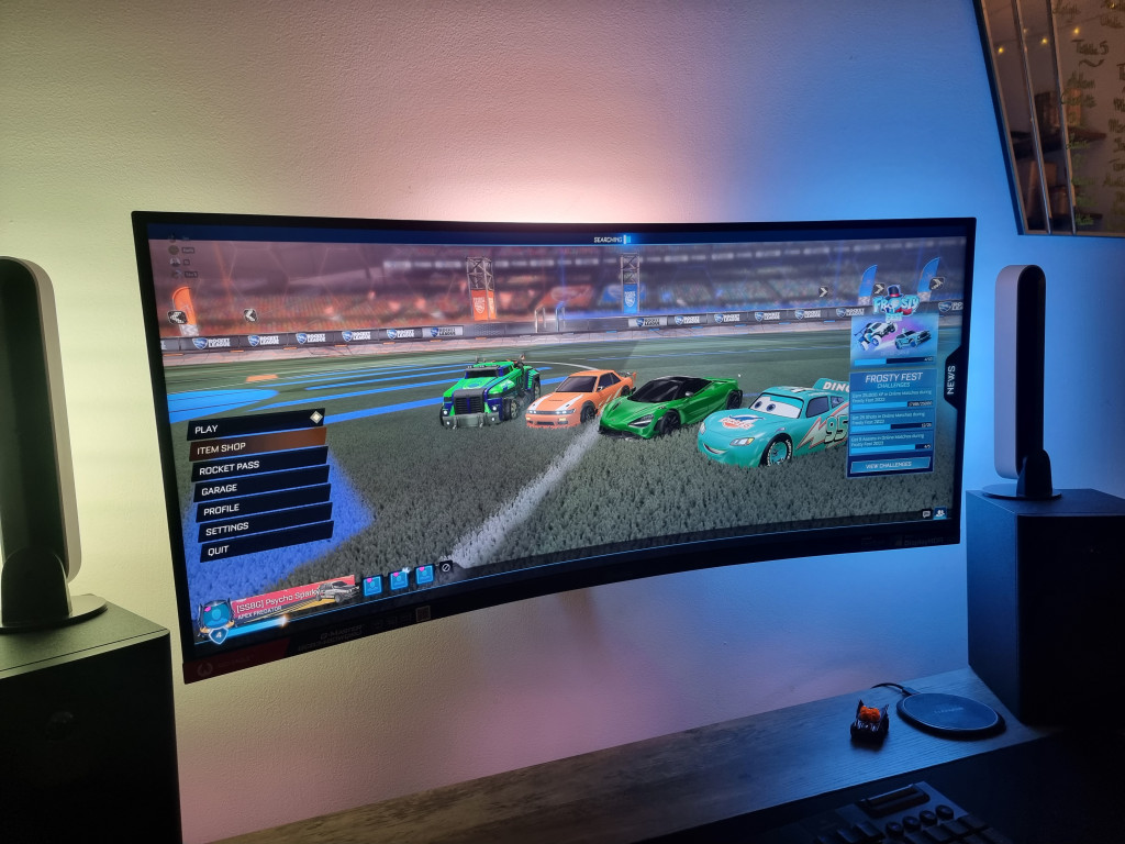 photo showing the iiyama monitor mounted to the wall. Rocket league is displayed. The monitor is serenaded by Phillips hue play bars that light around the wall behind the monitor witht he colours on the screen. left is green, top is orange and right is blue.