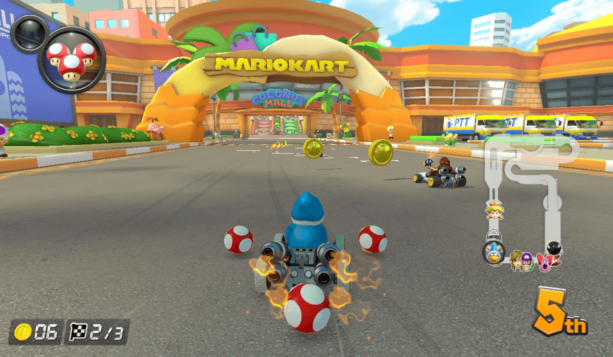 A screenshot of a race around Coconut Mall, a returning track added to Mario Kart 8 Deluxe by the Booster Course Pass. Racers are driving towards the finish line, which is just before the entrance to the eponymous mall.