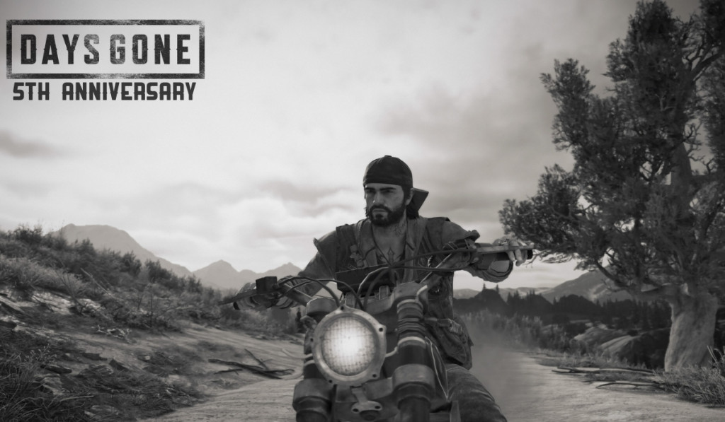 Black and white screenshot from Days Gone of main character Deacon riding a motorbike towards the camera on a rural road. The Days Gone logo is top left with text below reading "5th Anniversary"