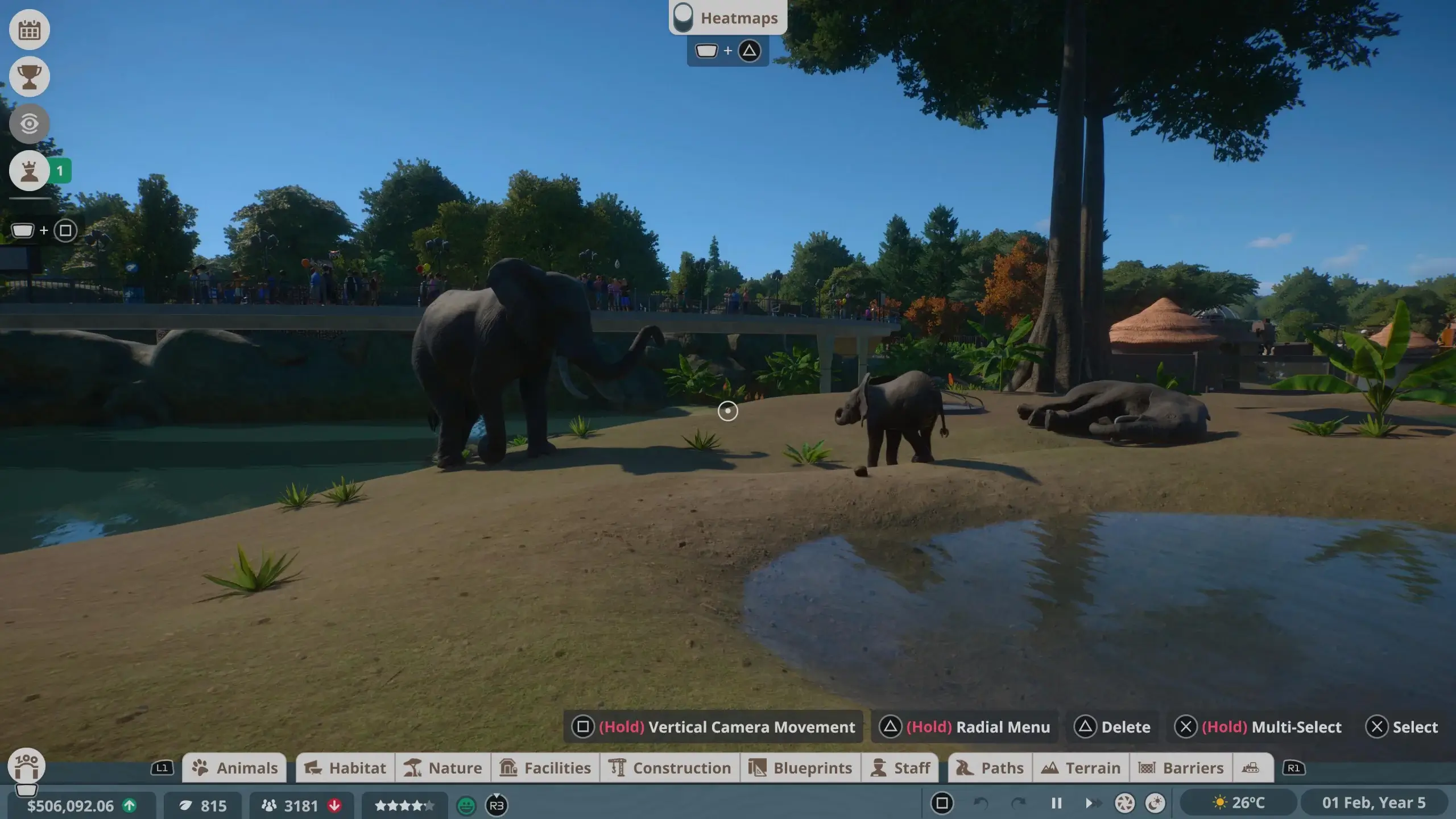 A close up of view of the elephant exhibit where 2 adults and a baby elephant have an area reminscient of their home with the terrain and water in their habitat. Also the Planet Zoo game menu along the bottom of the screen.