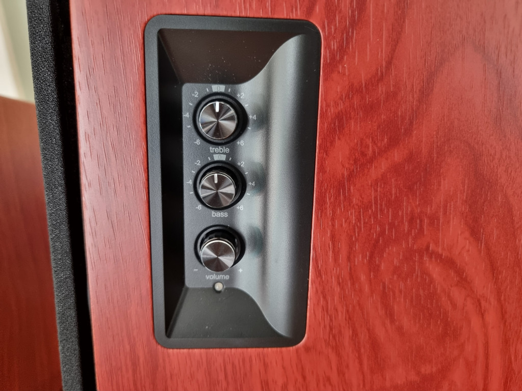 photo showing the side view of the powered righthand speaker. There are 3 black dials sunken into the rectangular shroud for bass, treble and volume controls.