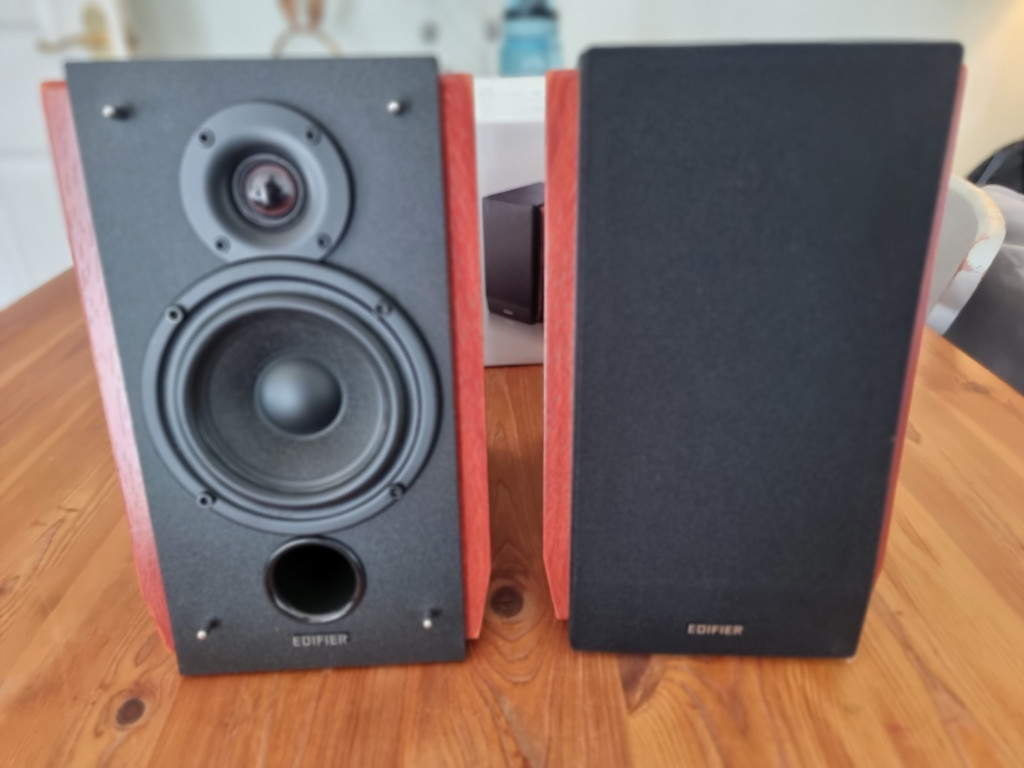 photo showing 2 edifier bookshelf speakers sitting on a wooden table. The front of the speakers are black and the enclosures are a walnut brown.