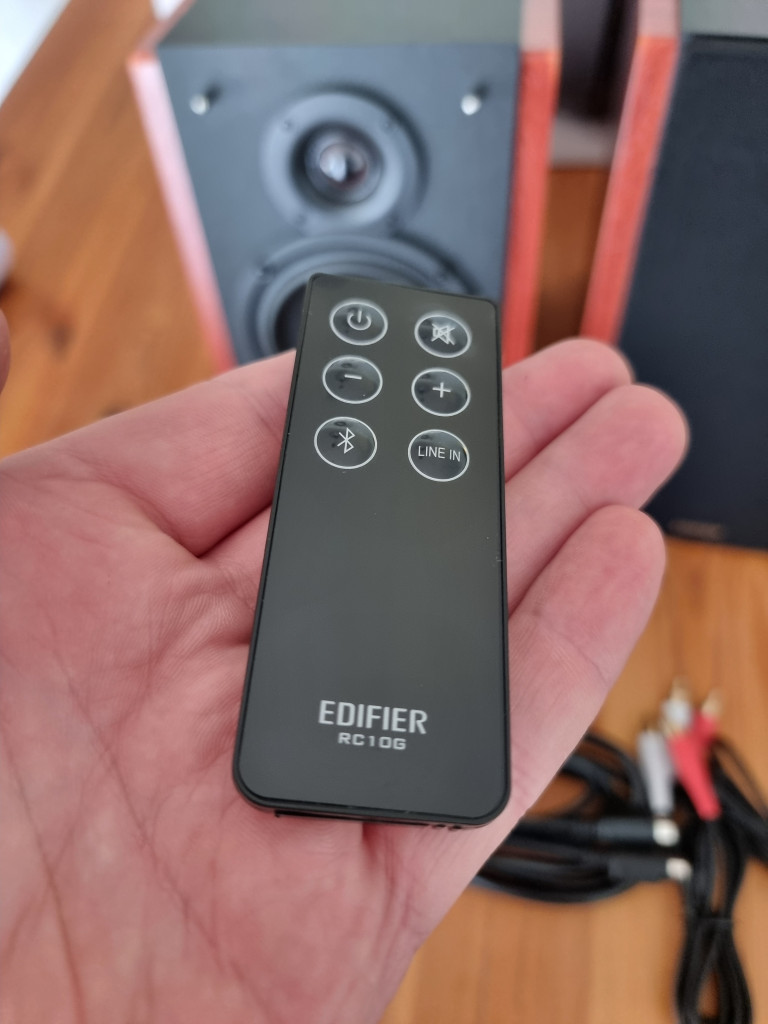 photo showing the Edifier remote control for the speakers. It is a small thin black rectangular piece of plastic with 6 depressible buttons to control power, signal and volume.