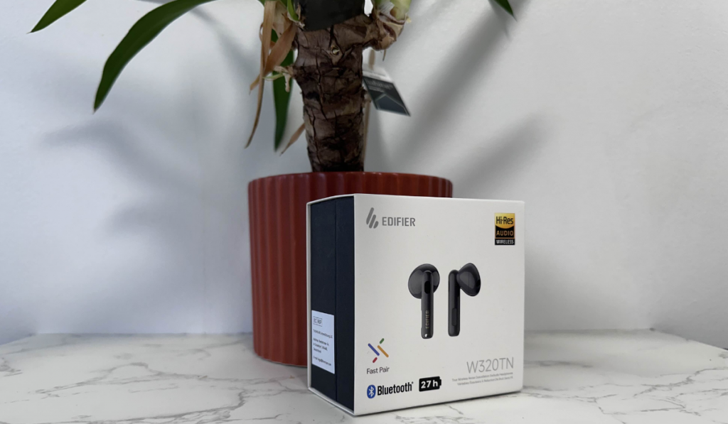 A boxed pair of Edifier W320TN sit on a white marble tabletop. Behind them is a household plant.