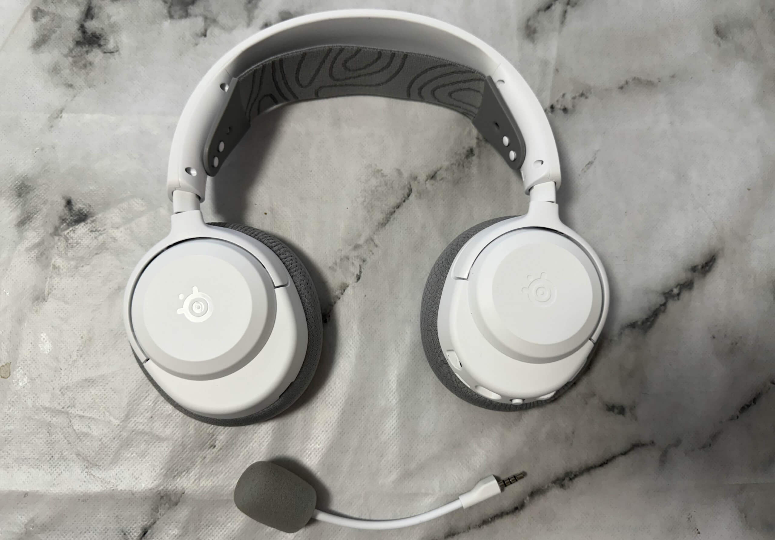 image of the arctis nova 3x wireless headset flat on the table, showing off the detachable microphone