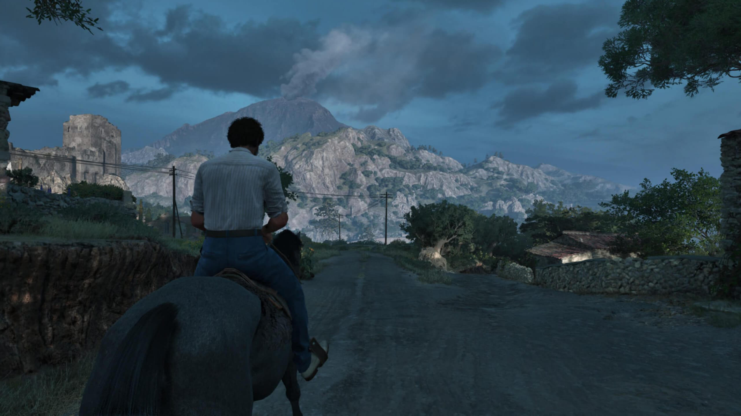 Screenshot from Mafia: The Old Country. A person rides a horse along a rural road towards a smoking volcano under a cloudy sky. The scene conveys a sense of adventure and impending action.