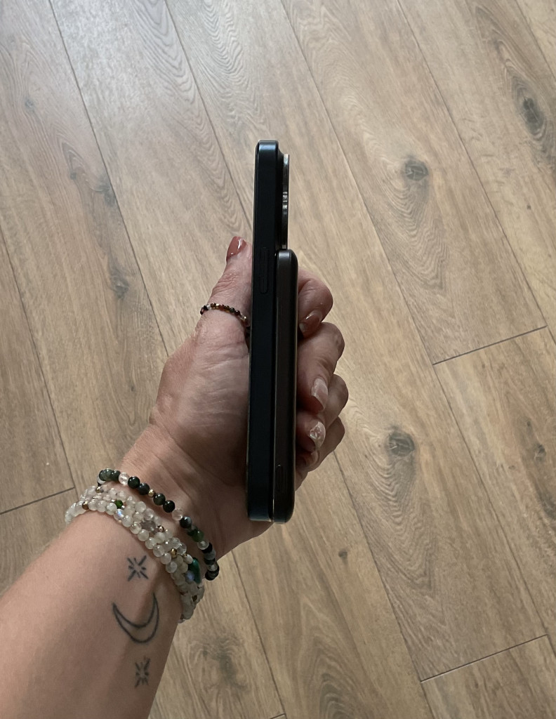 A person holds a smartphone horizontally, showcasing its thin profile of the Anker nano battery. Wrist adorned in colorful bracelets and a tattoo visible.
