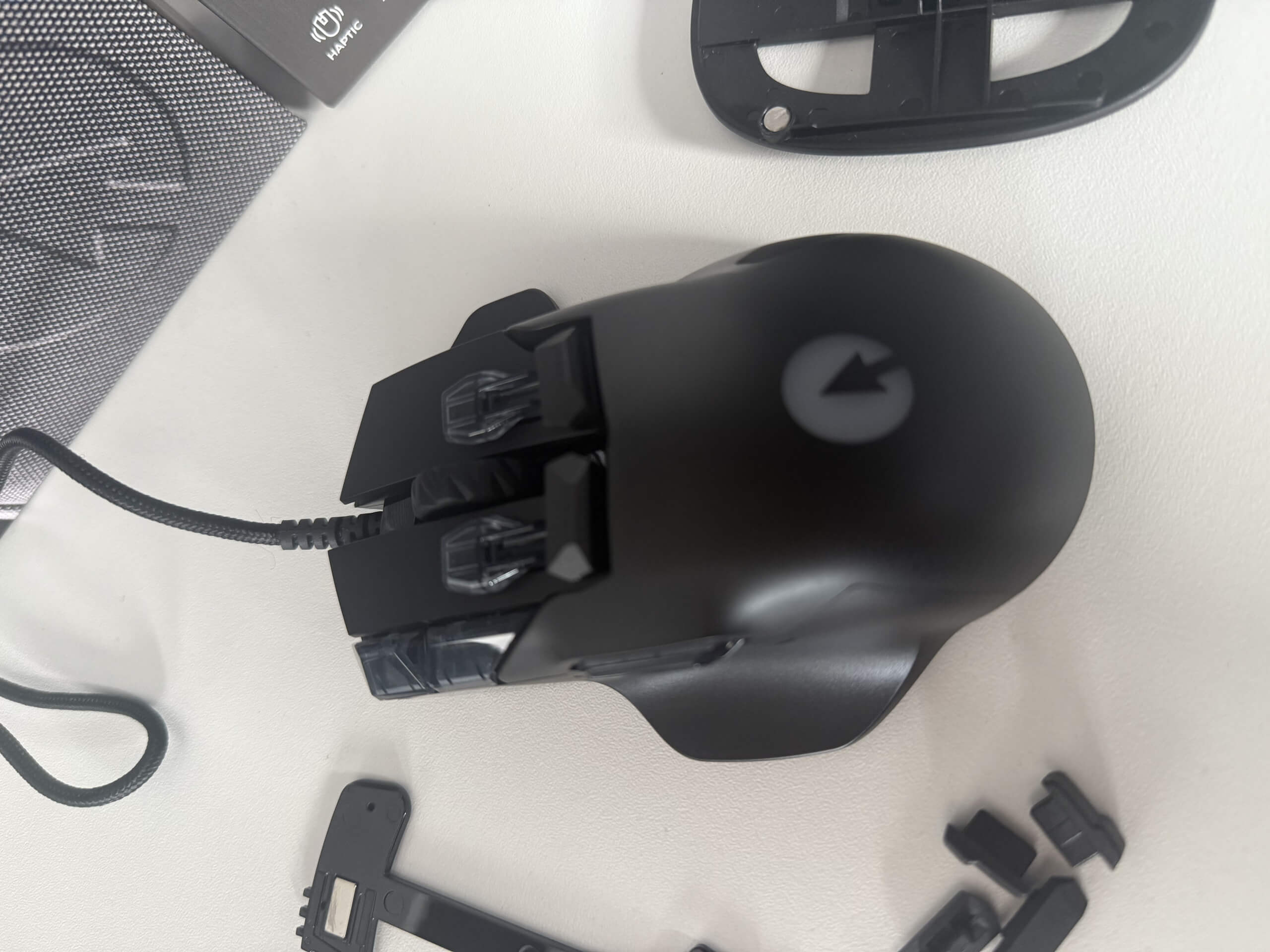 A black Swiftpoint Z2 gaming mouse with customizable buttons, accompanied by removable parts, sits on a white surface.