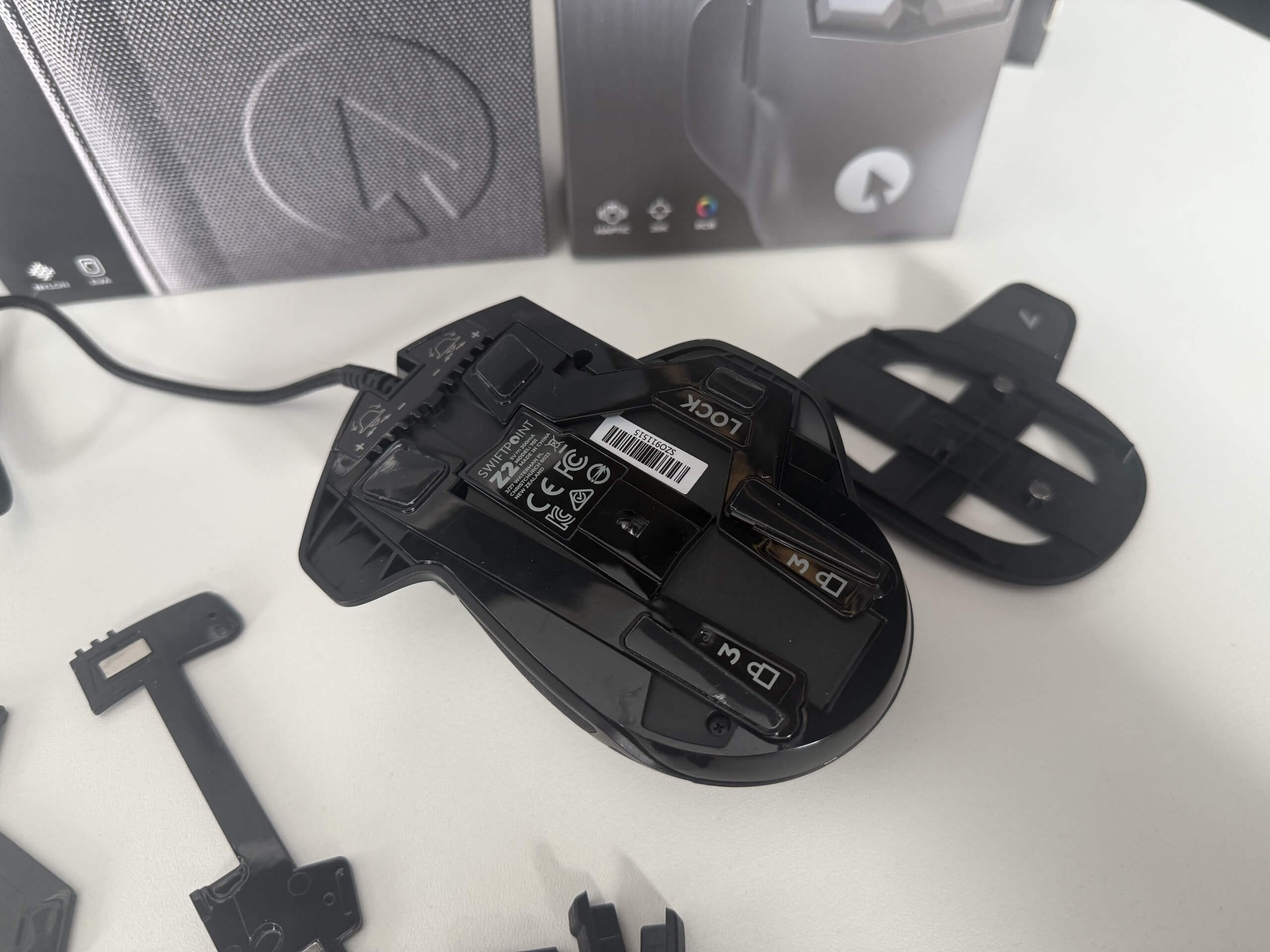 Close-up of a gaming mouse with removable parts and a USB cable, alongside its packaging on a white surface.