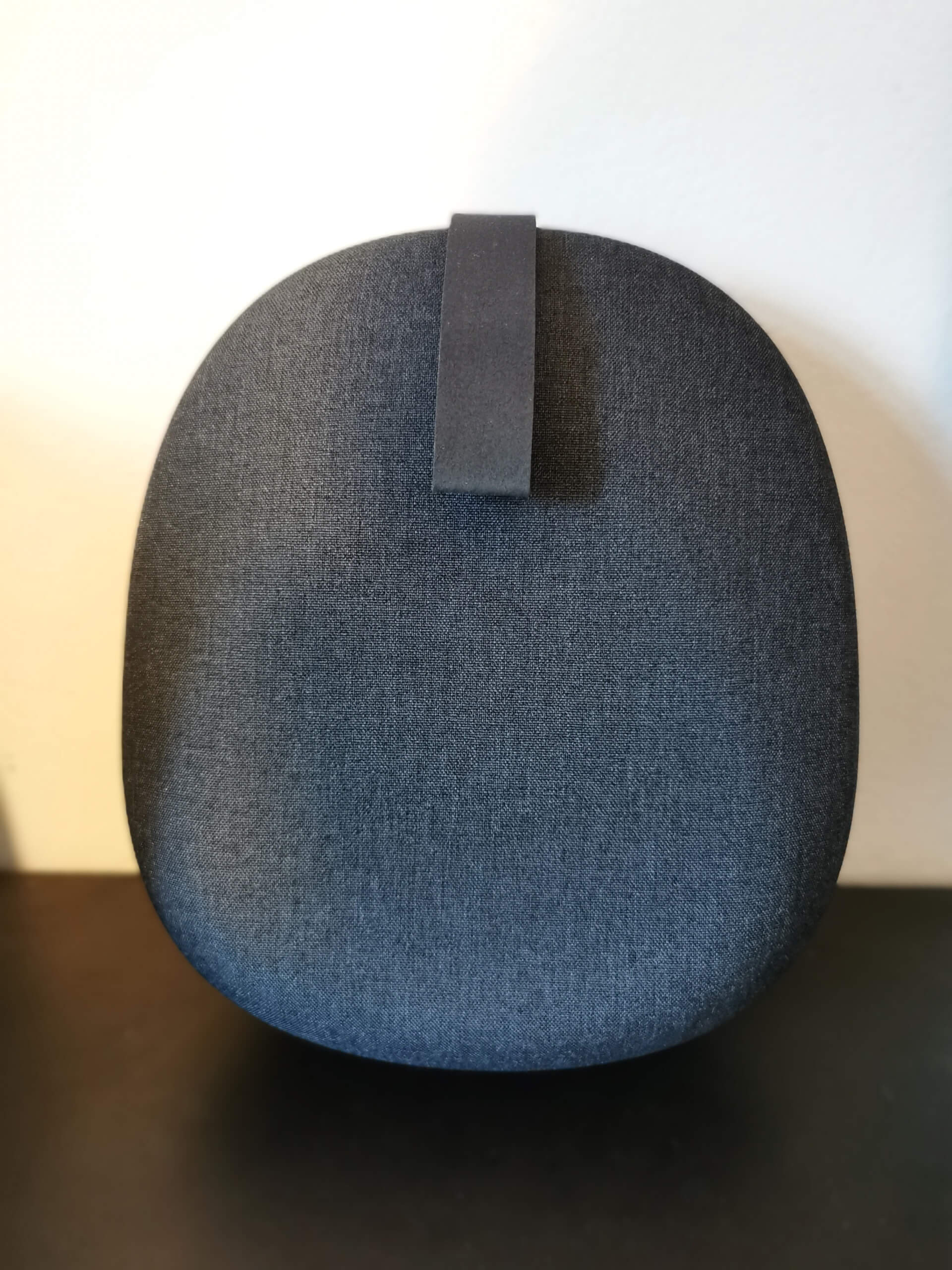 Sony WH-1000XM6 charcoal fabric case with carrying loop. Pictured lean against a white wall on a black desk.