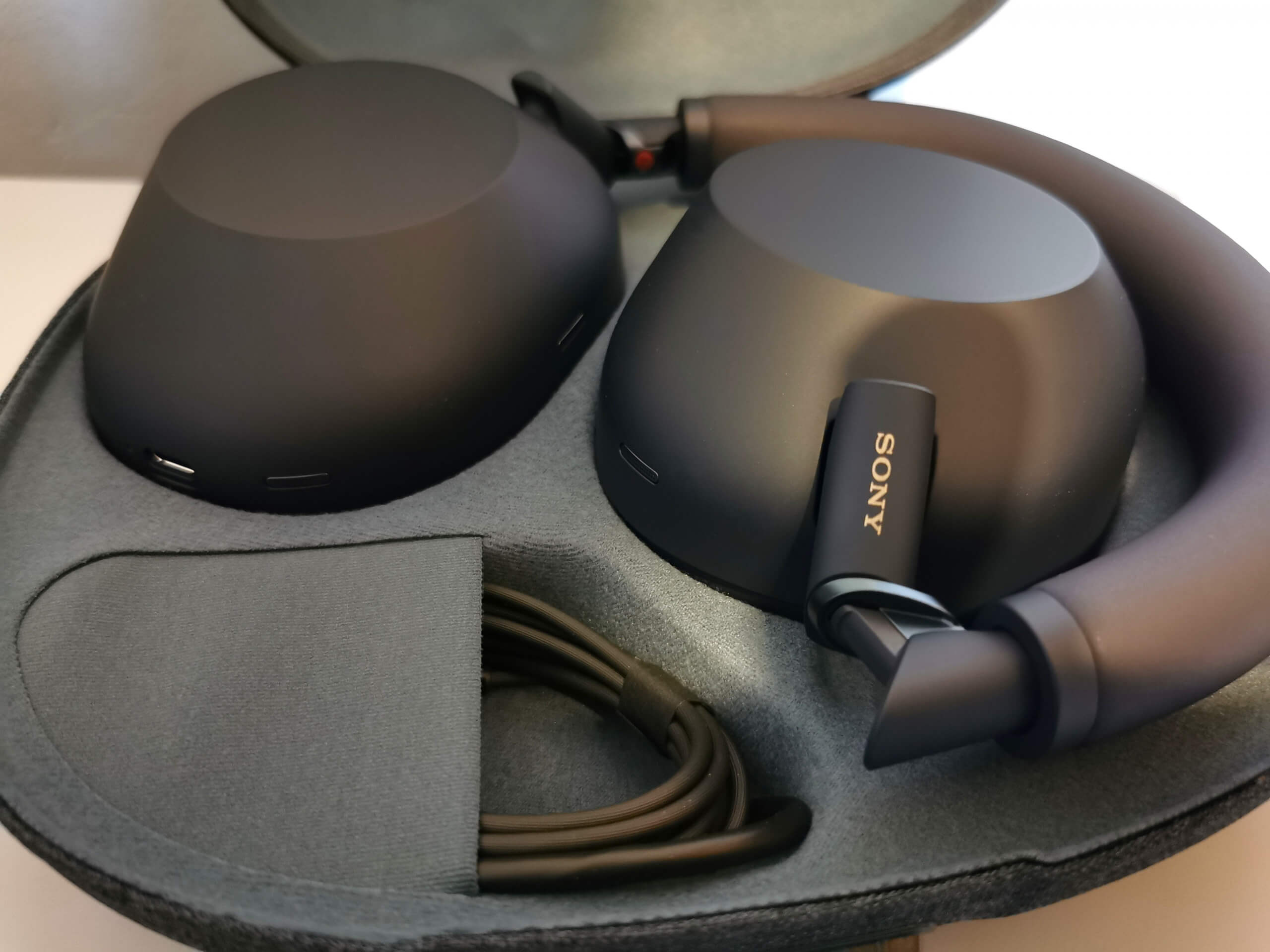 Midnight Blue Sony WH-1000XM6 pictured folded up inside the open carrying case. There is a small pouch inside the case that houses the charging small charging cable.