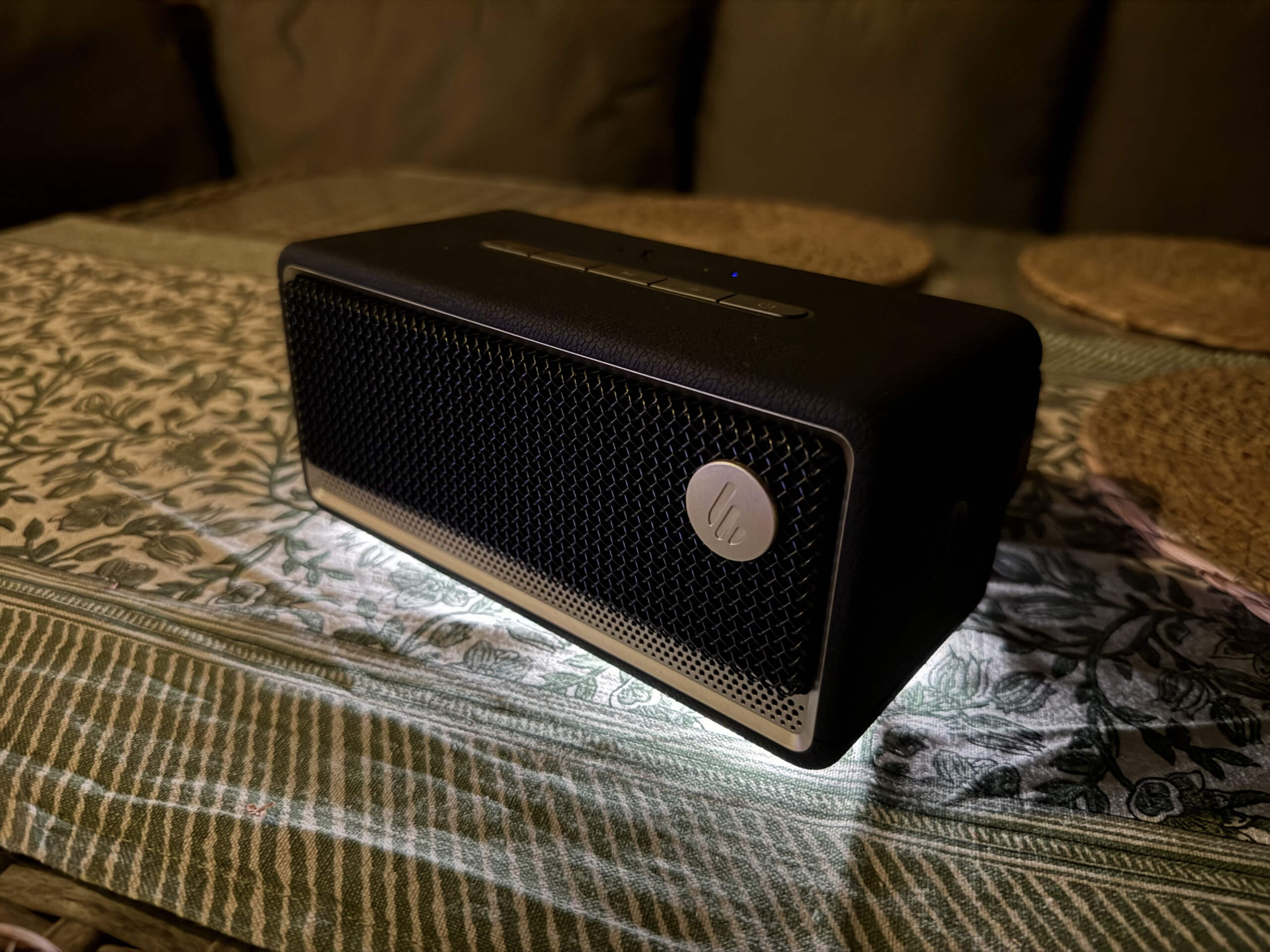 A sleek black portable speaker rests on a patterned tablecloth, illuminated by soft light, showcasing its modern design and texture.