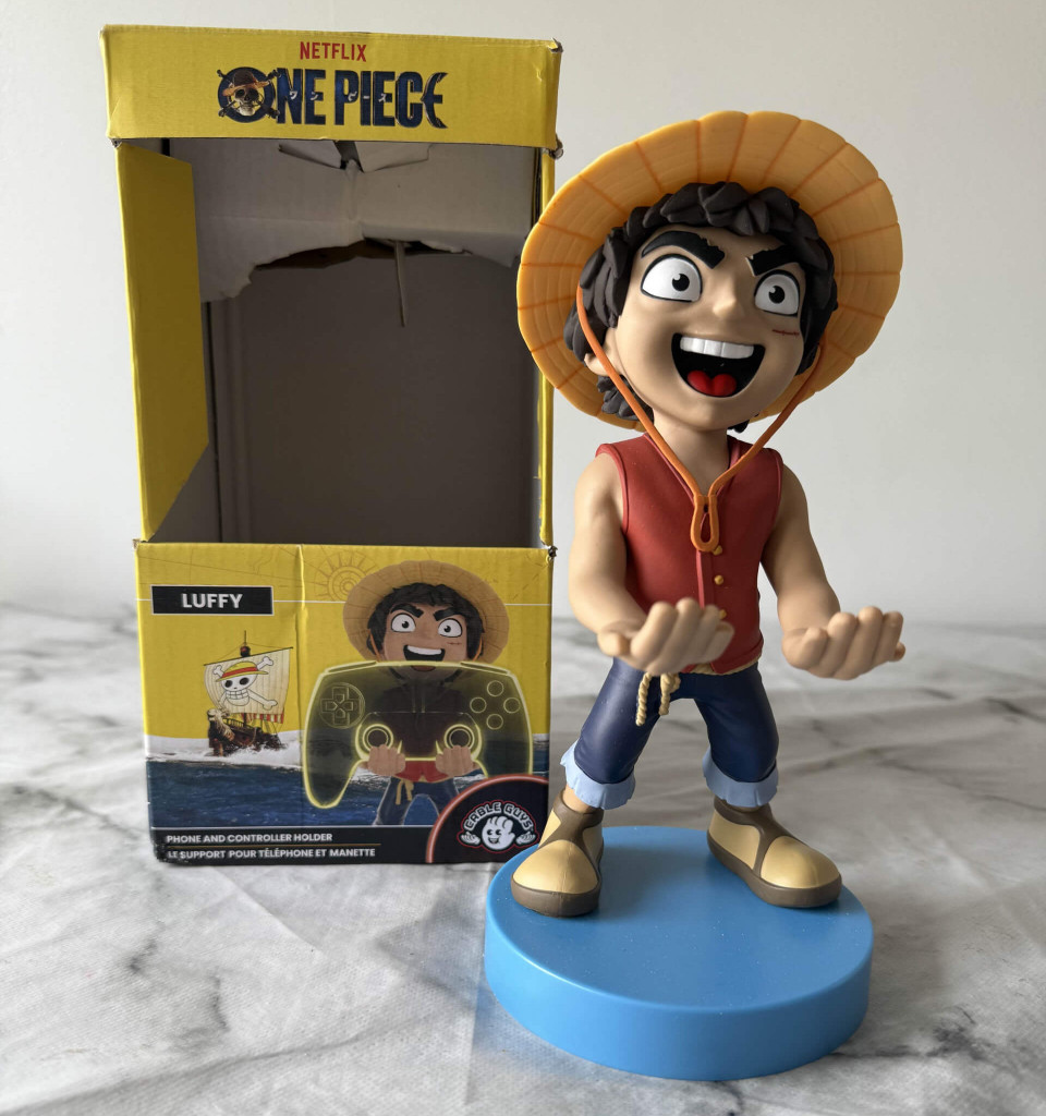 A cable guys figurine of a character from "One Piece," standing on a blue base, alongside a yellow box featuring illustrations related to the character.