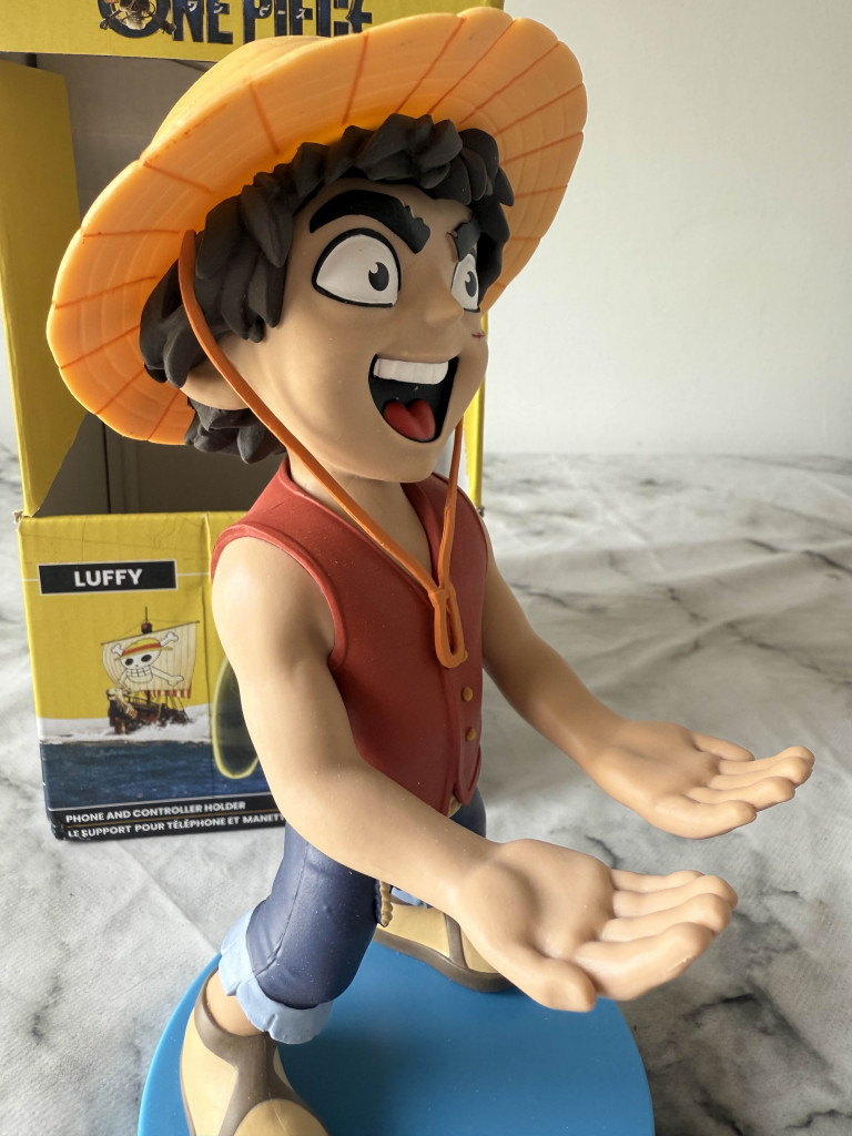 A Luffy figurine from One Piece, wearing a straw hat and red vest, stands on a blue base, arms extended as if inviting interaction.