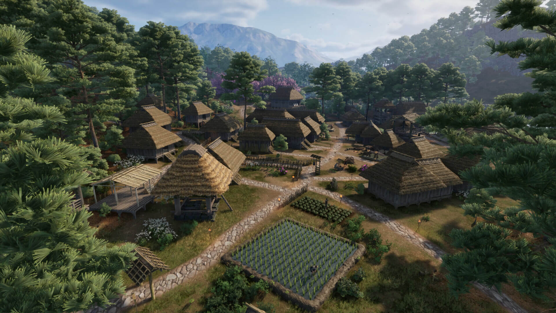 Screenshot from Sengoku Dynasty. A peaceful farming village, with farmers tending to the crops. The village consists of wooden structures featuring thatched roofs. A lush forest surrounds the buildings and a mountain range looms in the distance.