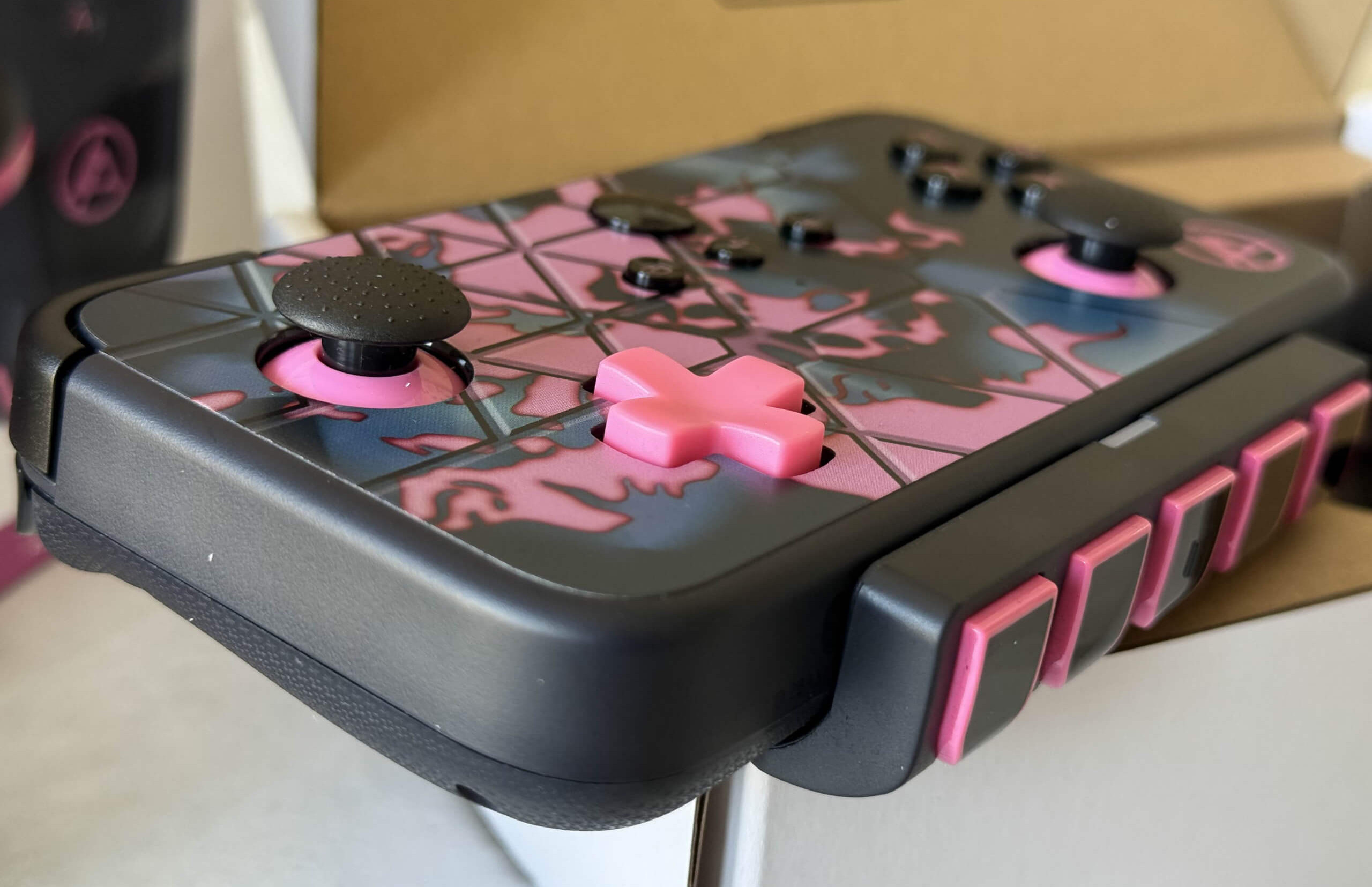 A close-up of linkin park neo s black and pink gaming controller featuring textured grips and multiple buttons, resting on a neutral background.